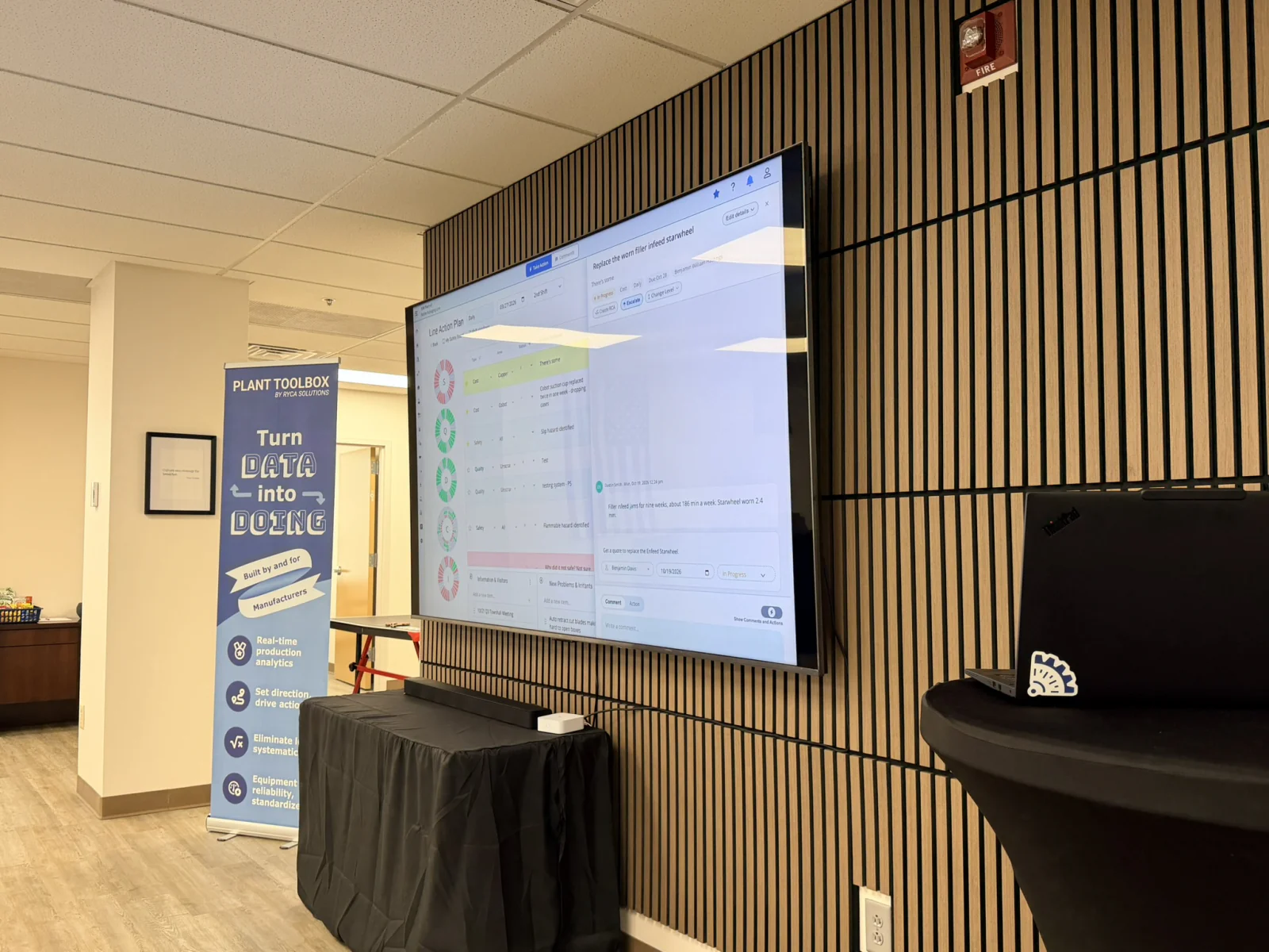 A Plant Toolbox line action plan on the large screen in the Collaboration center, mounted on a slatted wood wall beside a Plant Toolbox banner.